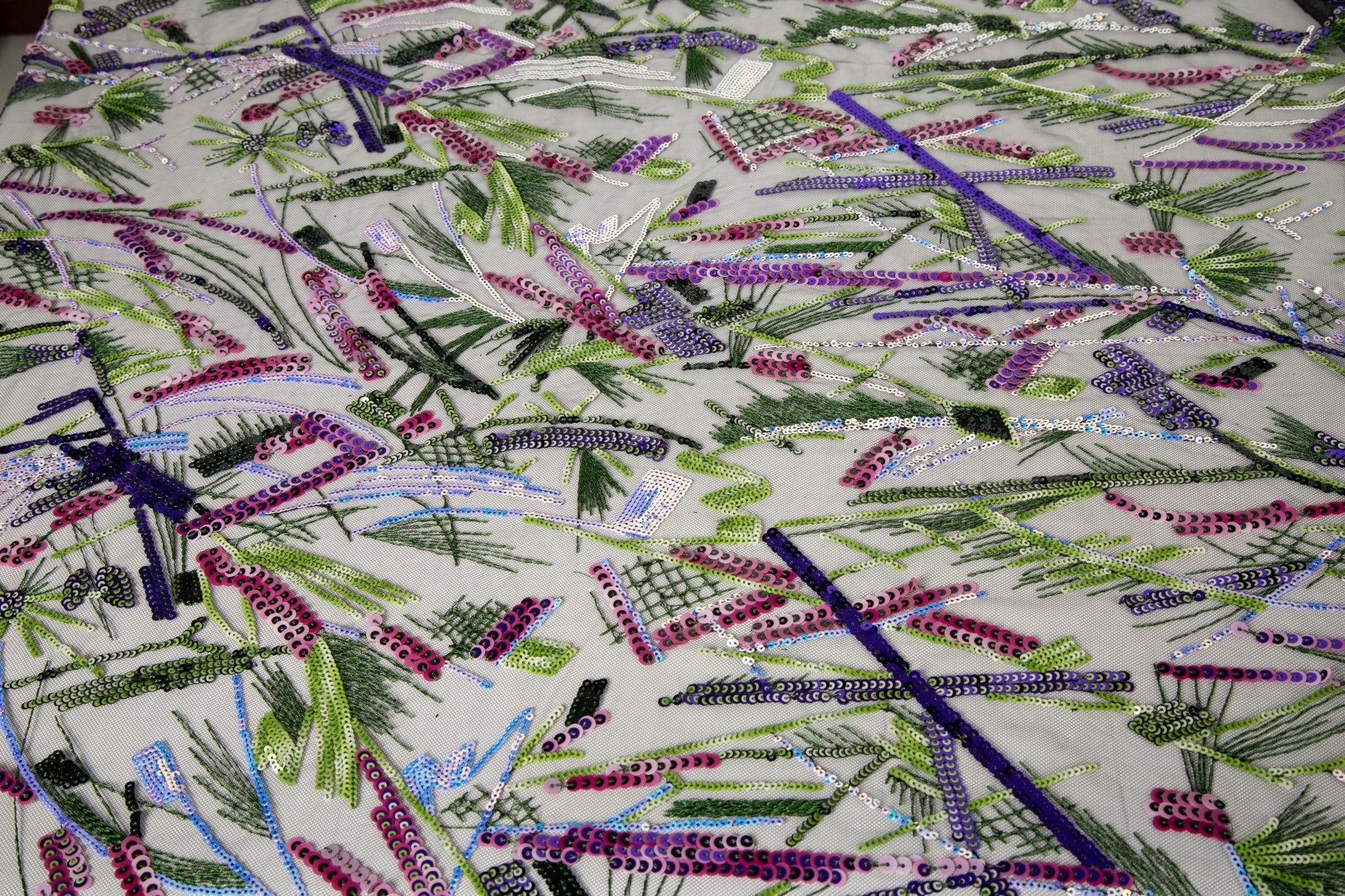 An abstract embroidery fabric on black tulle, with a graffiti-like pattern of lines made from neon green, pink, and purple sequins and thread.
