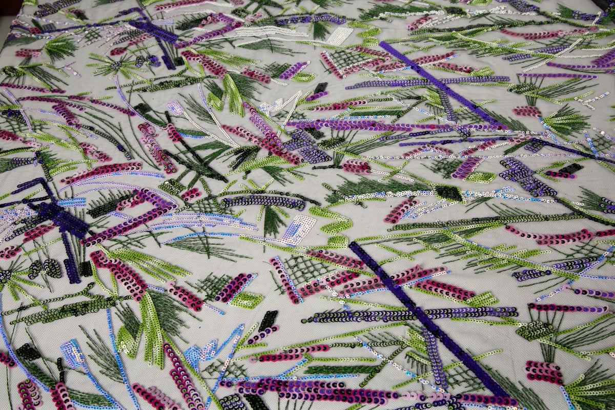 An abstract embroidery fabric on black tulle, with a graffiti-like pattern of lines made from neon green, pink, and purple sequins and thread.
