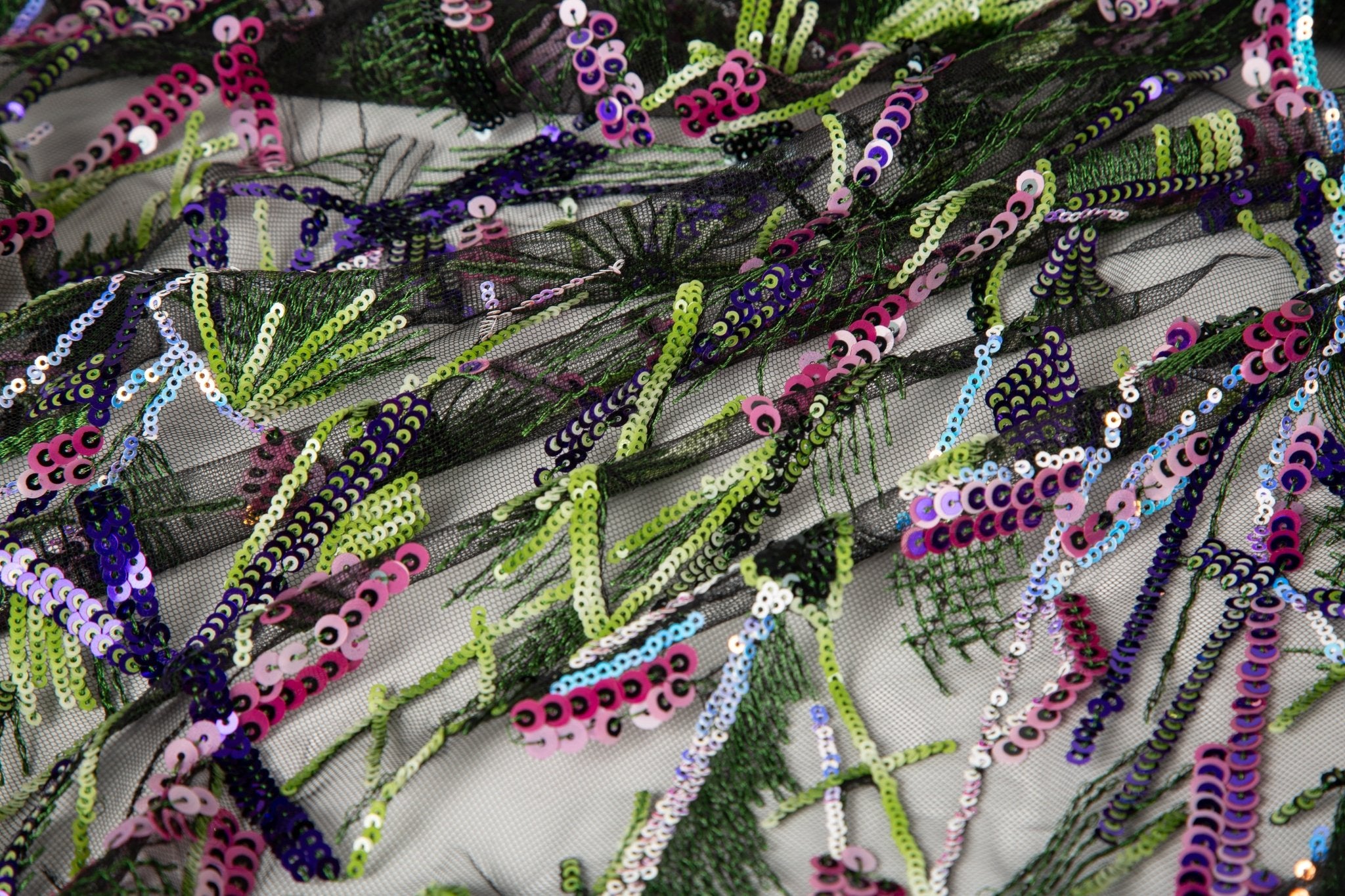 An abstract embroidery fabric on black tulle, with a graffiti-like pattern of lines made from neon green, pink, and purple sequins and thread.
