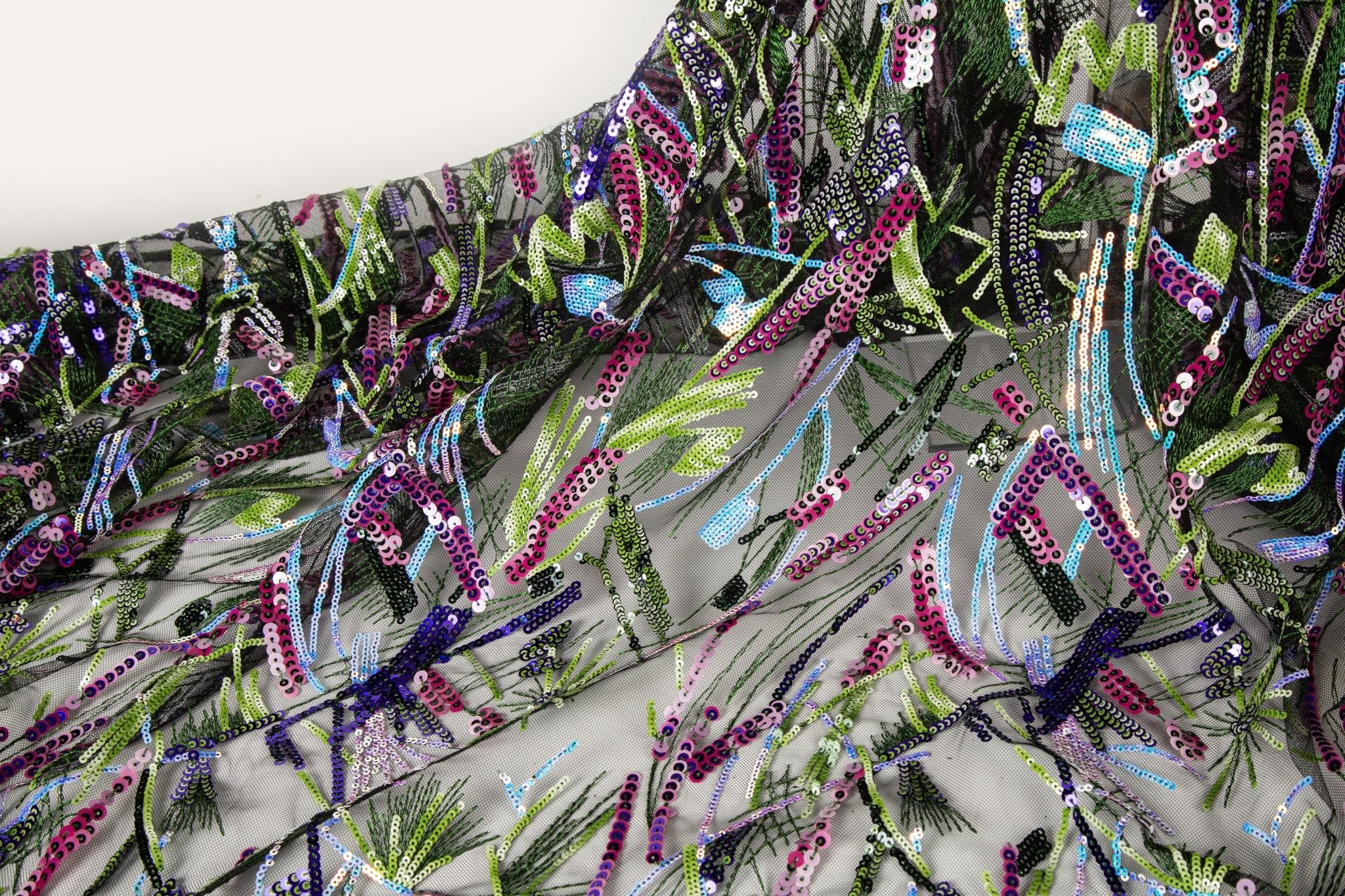 An abstract embroidery fabric on black tulle, with a graffiti-like pattern of lines made from neon green, pink, and purple sequins and thread.

