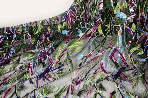 An abstract embroidery fabric on black tulle, with a graffiti-like pattern of lines made from neon green, pink, and purple sequins and thread.
