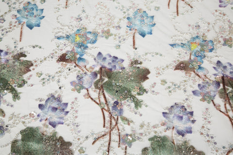 An embroidery fabric on ivory mesh, with a painterly pattern of water lilies in a blue and purple palette.
