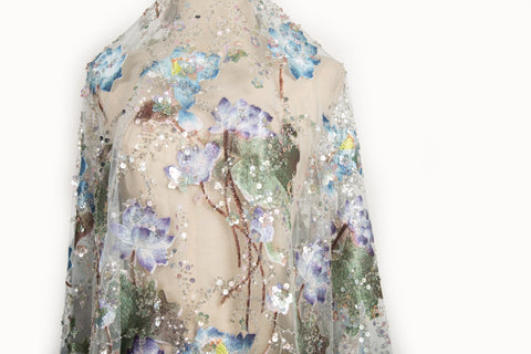 An embroidery fabric on ivory mesh, with a painterly pattern of water lilies in a blue and purple palette.
