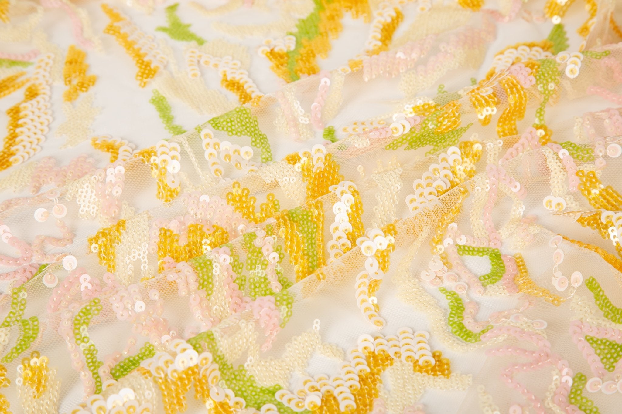 An abstract sequin embroidery fabric with a wavy pattern in yellow, pink, and green.
