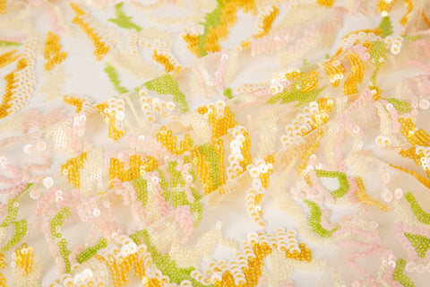 An abstract sequin embroidery fabric with a wavy pattern in yellow, pink, and green.

