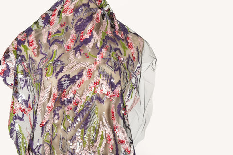 An abstract sequin embroidery fabric on a black base, with a wavy pattern in purple, pink, and green.
