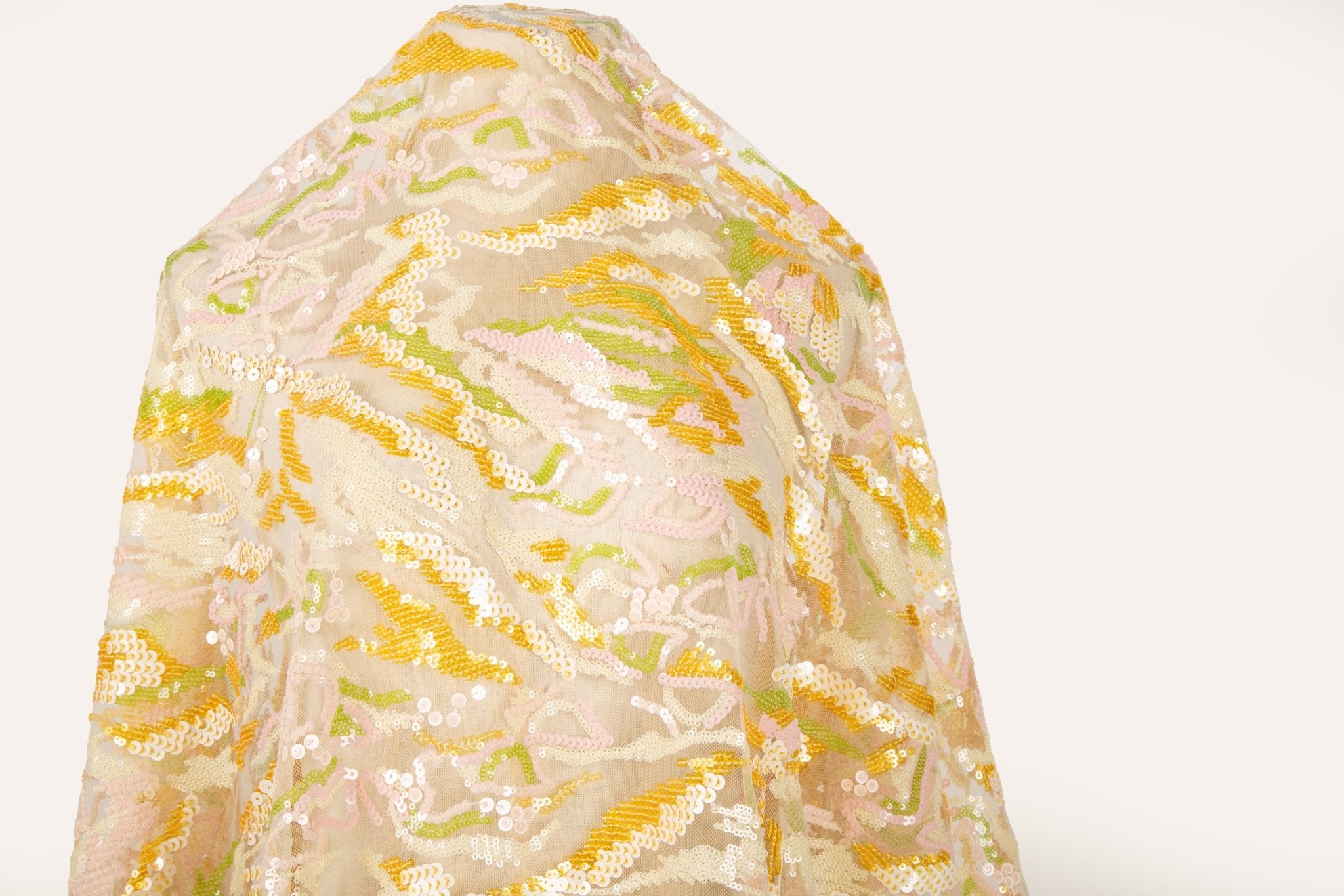 An abstract sequin embroidery fabric with a wavy pattern in yellow, pink, and green.
