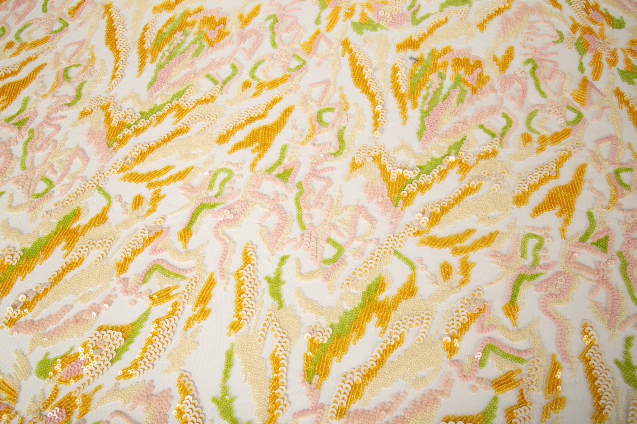  An abstract sequin embroidery fabric with a wavy pattern in yellow, pink, and green.
