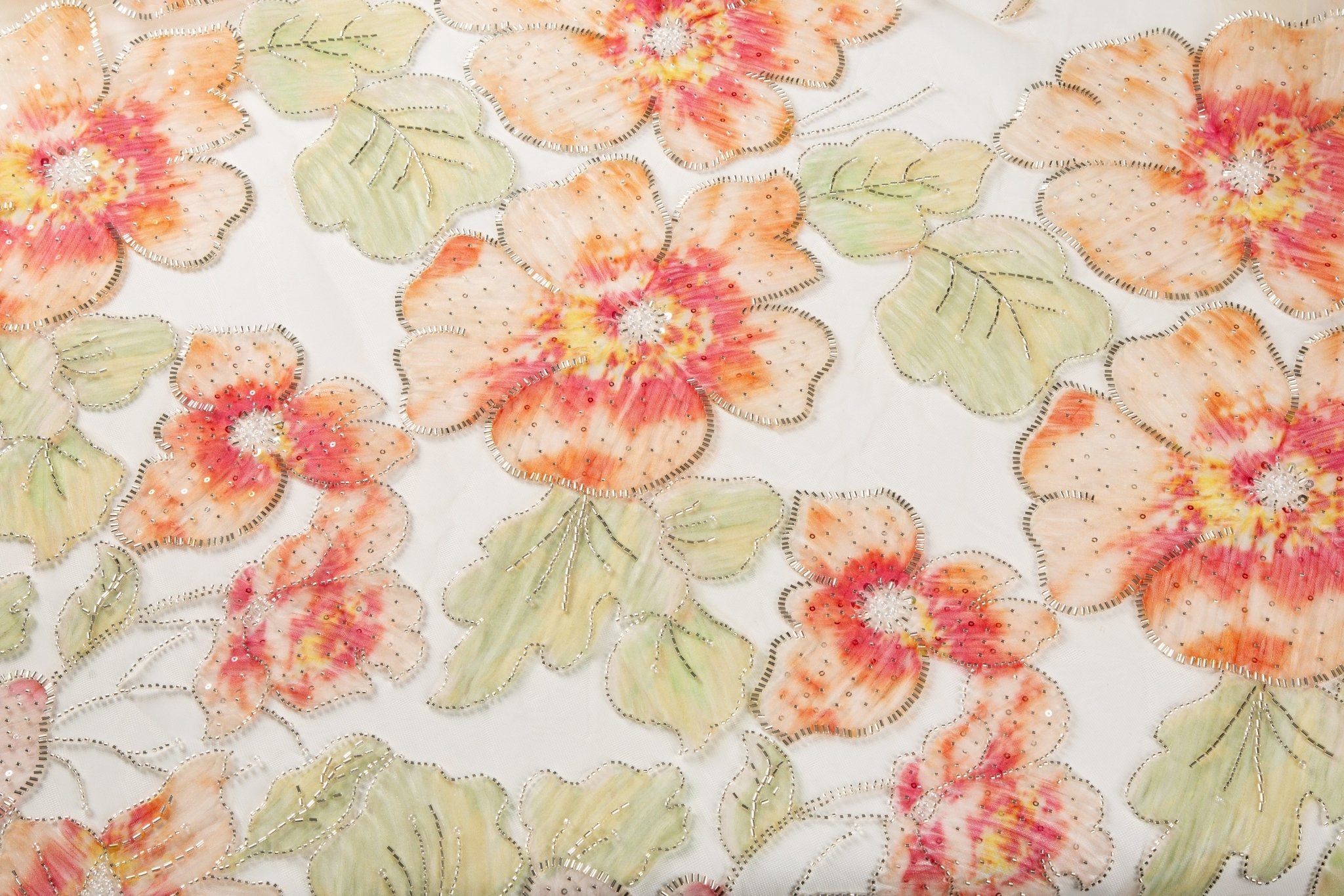 A luxurious floral fabric made with ribbon embroidery, featuring coral-colored flowers and green leaves.
