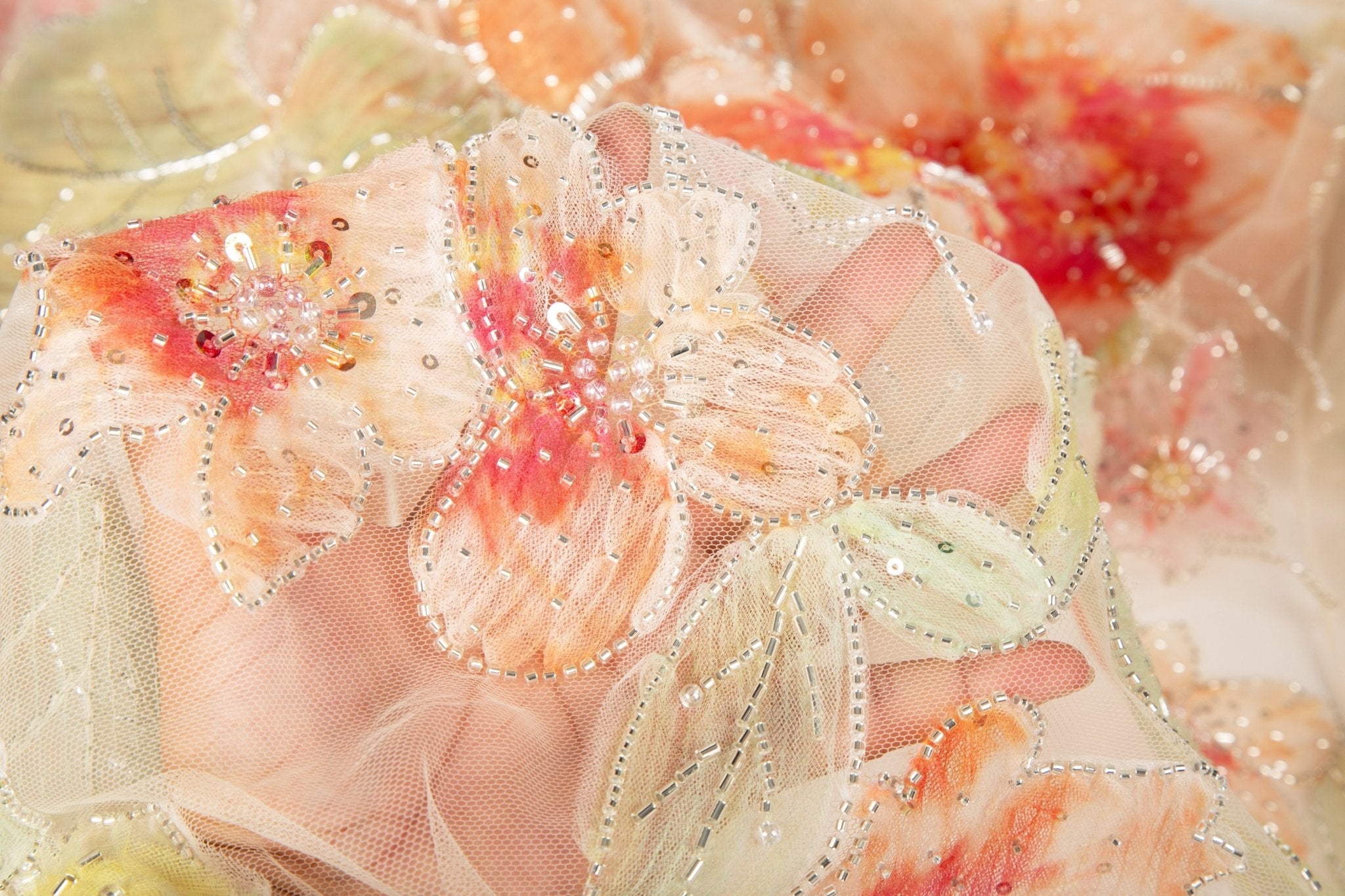 A luxurious floral fabric made with ribbon embroidery, featuring coral-colored flowers and green leaves.
