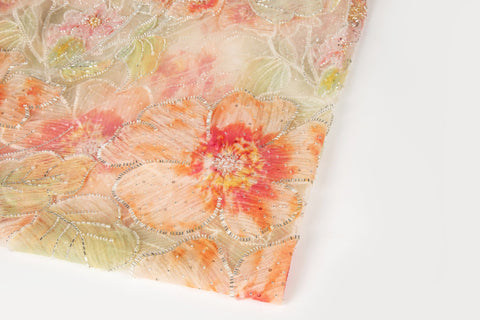 A luxurious floral fabric made with ribbon embroidery, featuring coral-colored flowers and green leaves.
