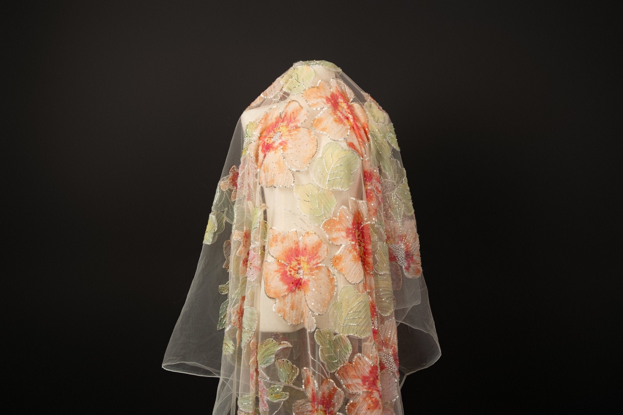 A luxurious floral fabric made with ribbon embroidery, featuring coral-colored flowers and green leaves.
