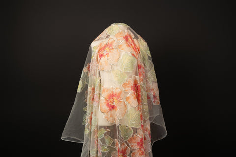 A luxurious floral fabric made with ribbon embroidery, featuring coral-colored flowers and green leaves.
