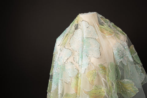 A luxurious fabric made with ribbon embroidery, featuring a large-scale leaf pattern in shades of mint green and blue.
