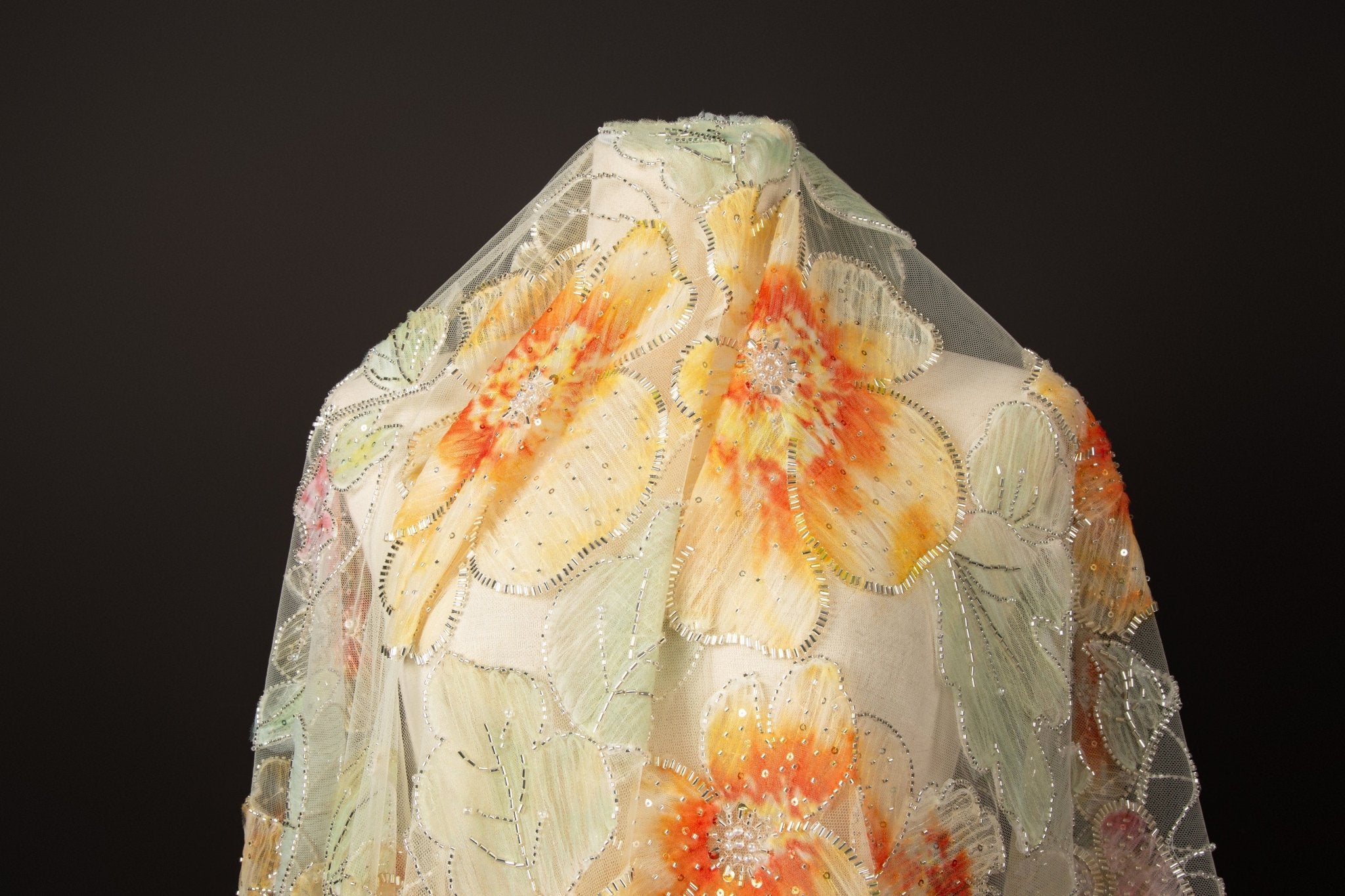 A luxurious fabric made with ribbon embroidery, featuring large-scale, yellow and orange flowers with green leaves.
