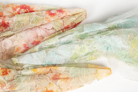    A luxurious fabric made with ribbon embroidery, featuring a large-scale leaf pattern in shades of mint green and blue.
   A luxurious floral fabric made with ribbon embroidery, featuring coral-colored flowers and green leaves.
   A luxurious fabric made with ribbon embroidery, featuring large-scale, yellow and orange flowers with green leaves.

