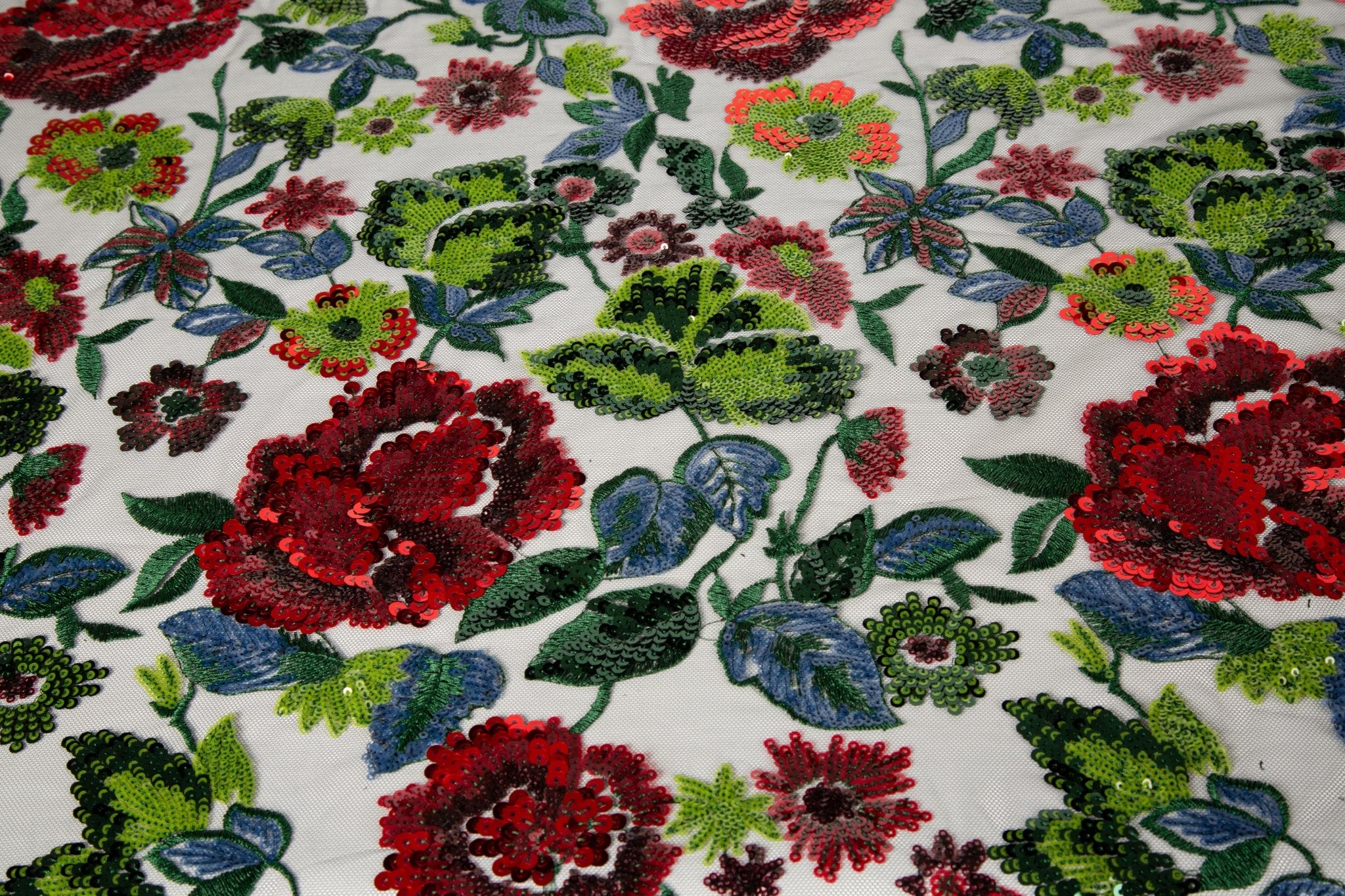 A sequin floral embroidery fabric on a black base, with red and green motifs.