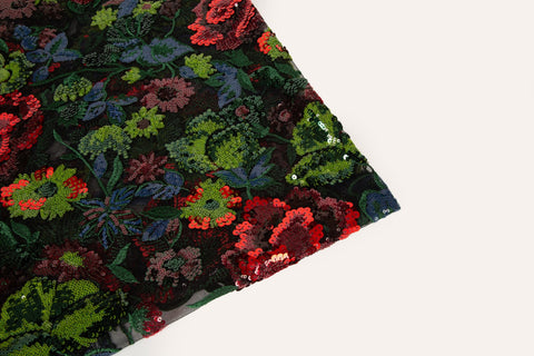 A sequin floral embroidery fabric on a black base, with red and green motifs.