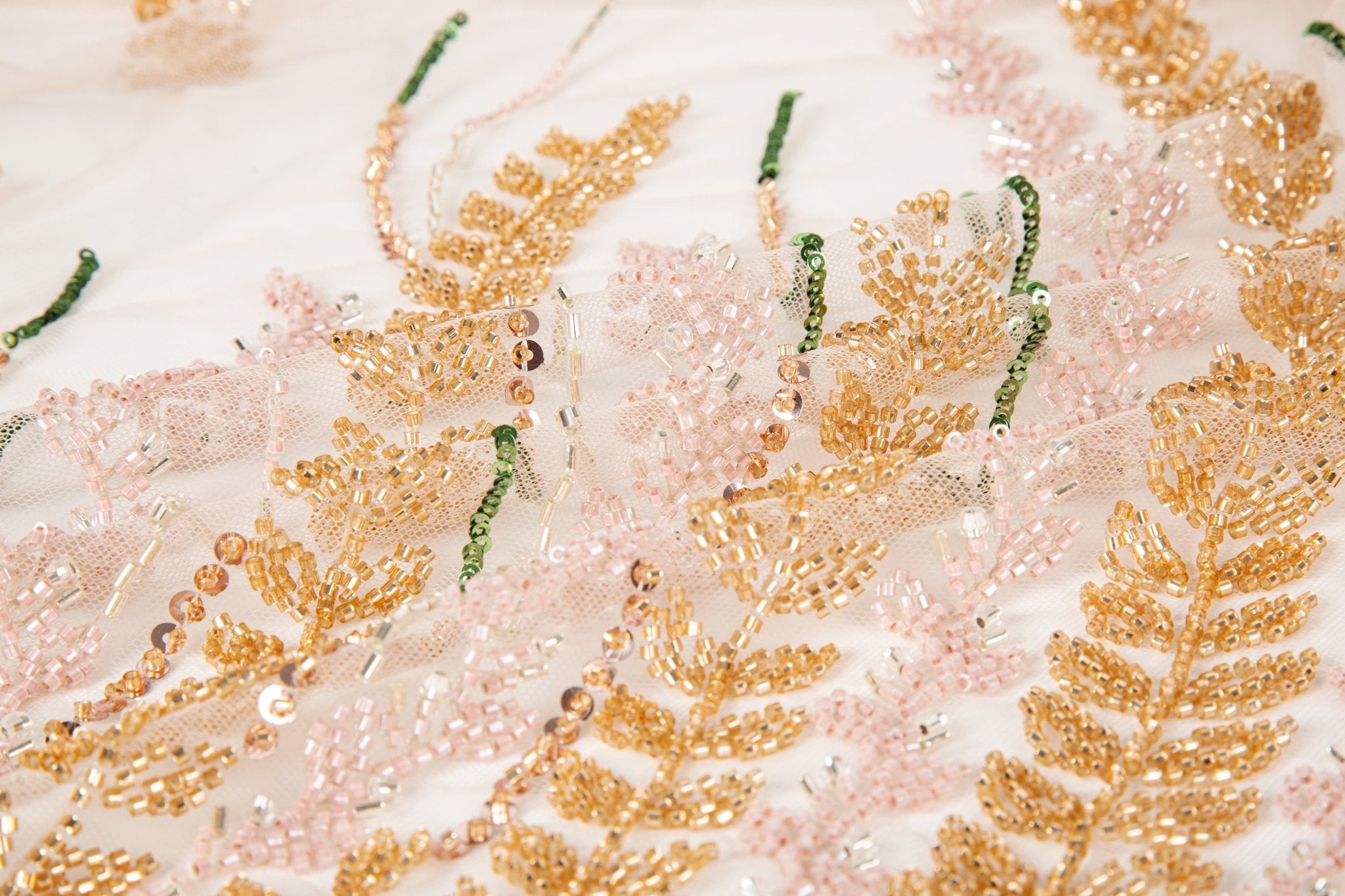 A hand-beaded embroidery fabric, with a vertical, wavy pattern of laurel leaves in rose gold, pink, and green.
