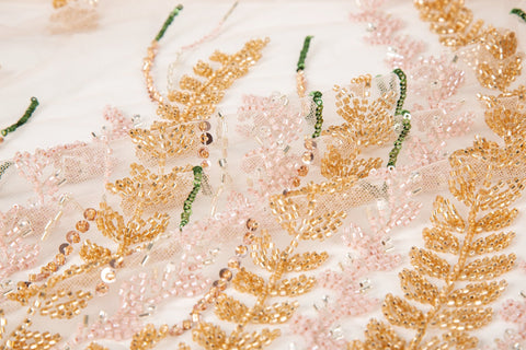 A hand-beaded embroidery fabric, with a vertical, wavy pattern of laurel leaves in rose gold, pink, and green.
