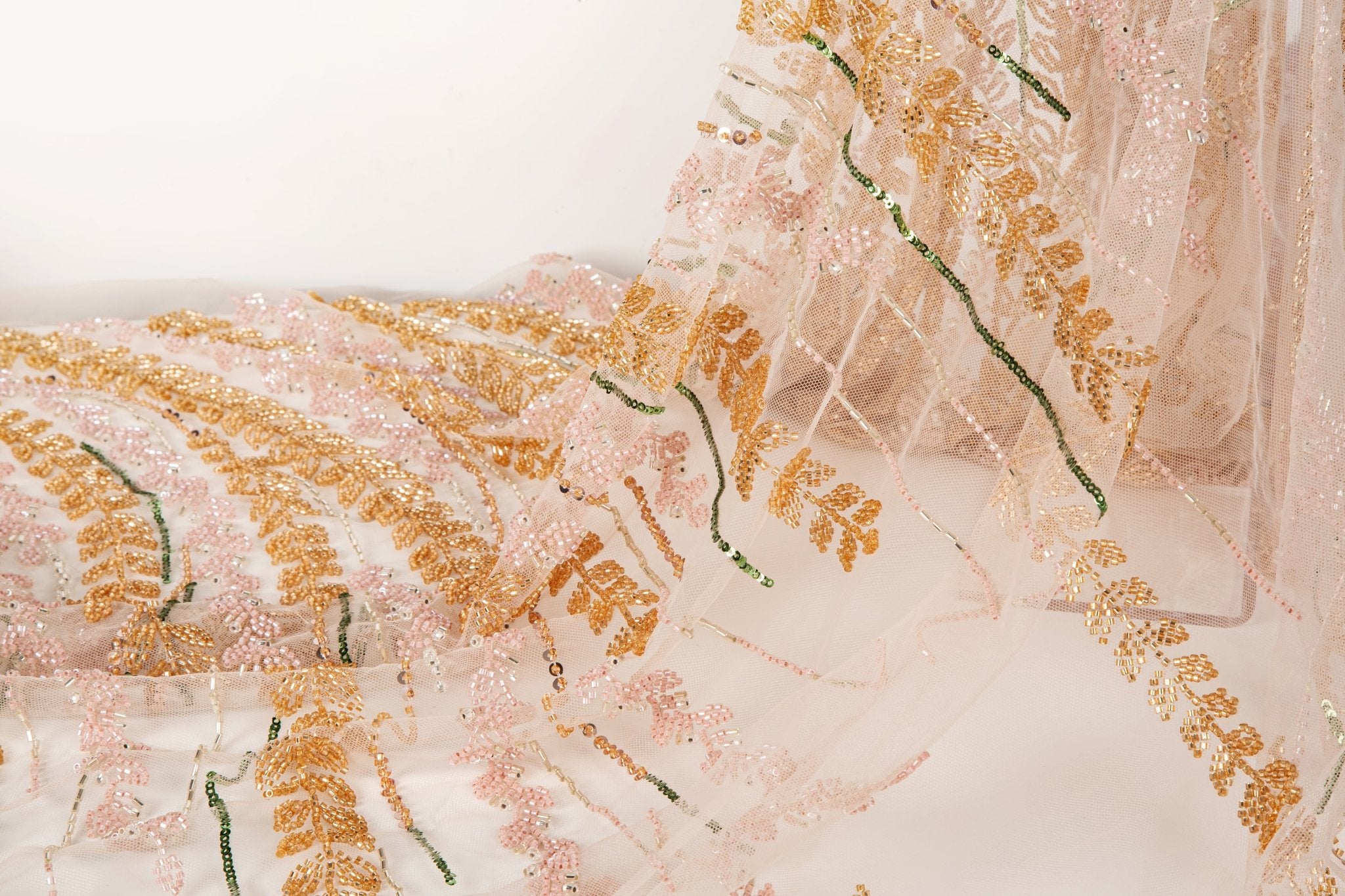A hand-beaded embroidery fabric, with a vertical, wavy pattern of laurel leaves in rose gold, pink, and green.
