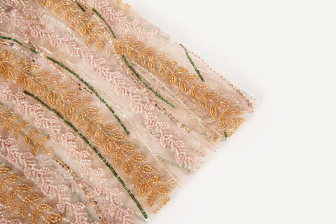 A hand-beaded embroidery fabric, with a vertical, wavy pattern of laurel leaves in rose gold, pink, and green.
