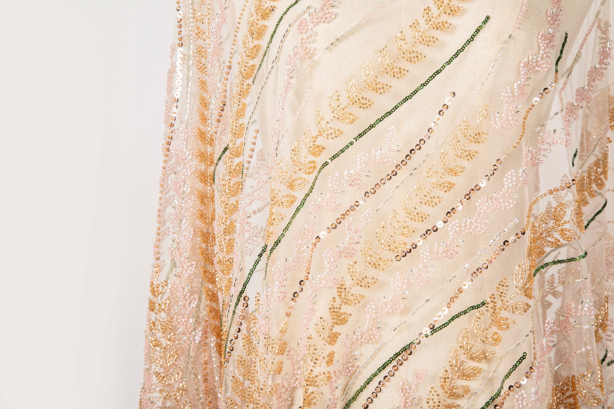 A hand-beaded embroidery fabric, with a vertical, wavy pattern of laurel leaves in rose gold, pink, and green.
