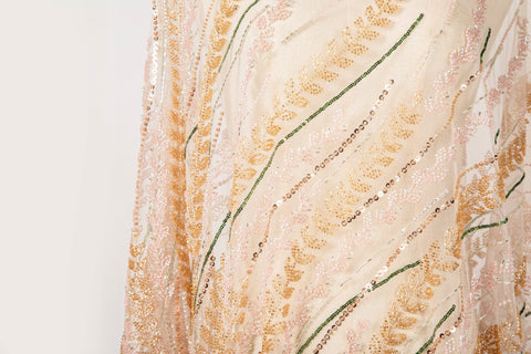 A hand-beaded embroidery fabric, with a vertical, wavy pattern of laurel leaves in rose gold, pink, and green.
