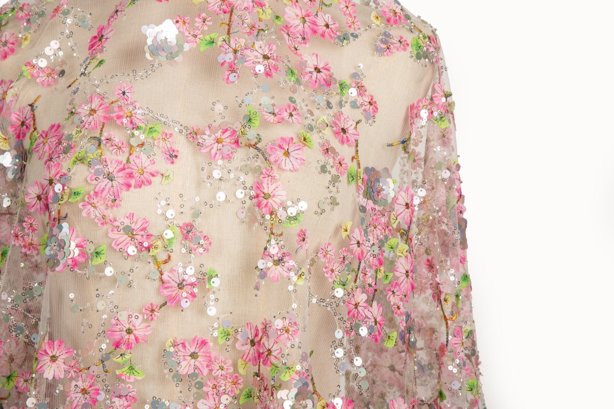 A fine embroidery fabric on white tulle, with a pattern of pink cherry blossom branches and shimmering sequins.

