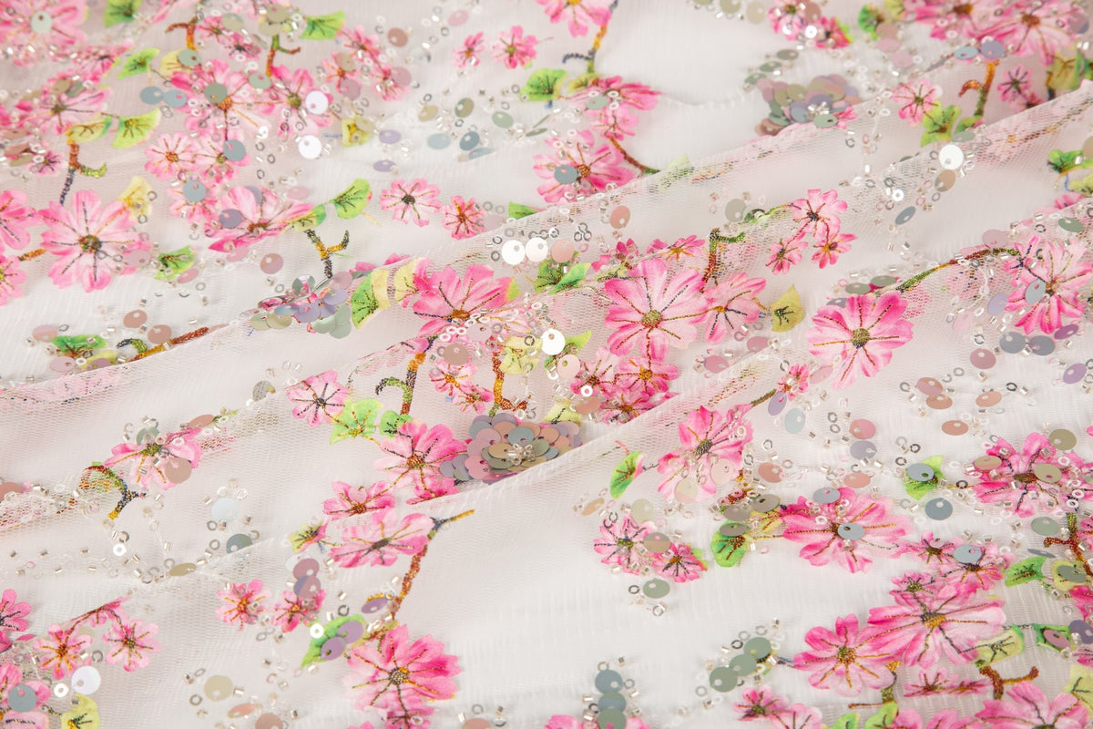 A fine embroidery fabric on white tulle, with a pattern of pink cherry blossom branches and shimmering sequins.
