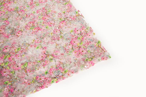 A fine embroidery fabric on white tulle, with a pattern of pink cherry blossom branches and shimmering sequins.
