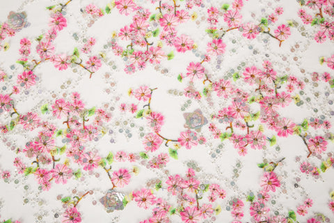 A fine embroidery fabric on white tulle, with a pattern of pink cherry blossom branches and shimmering sequins.
