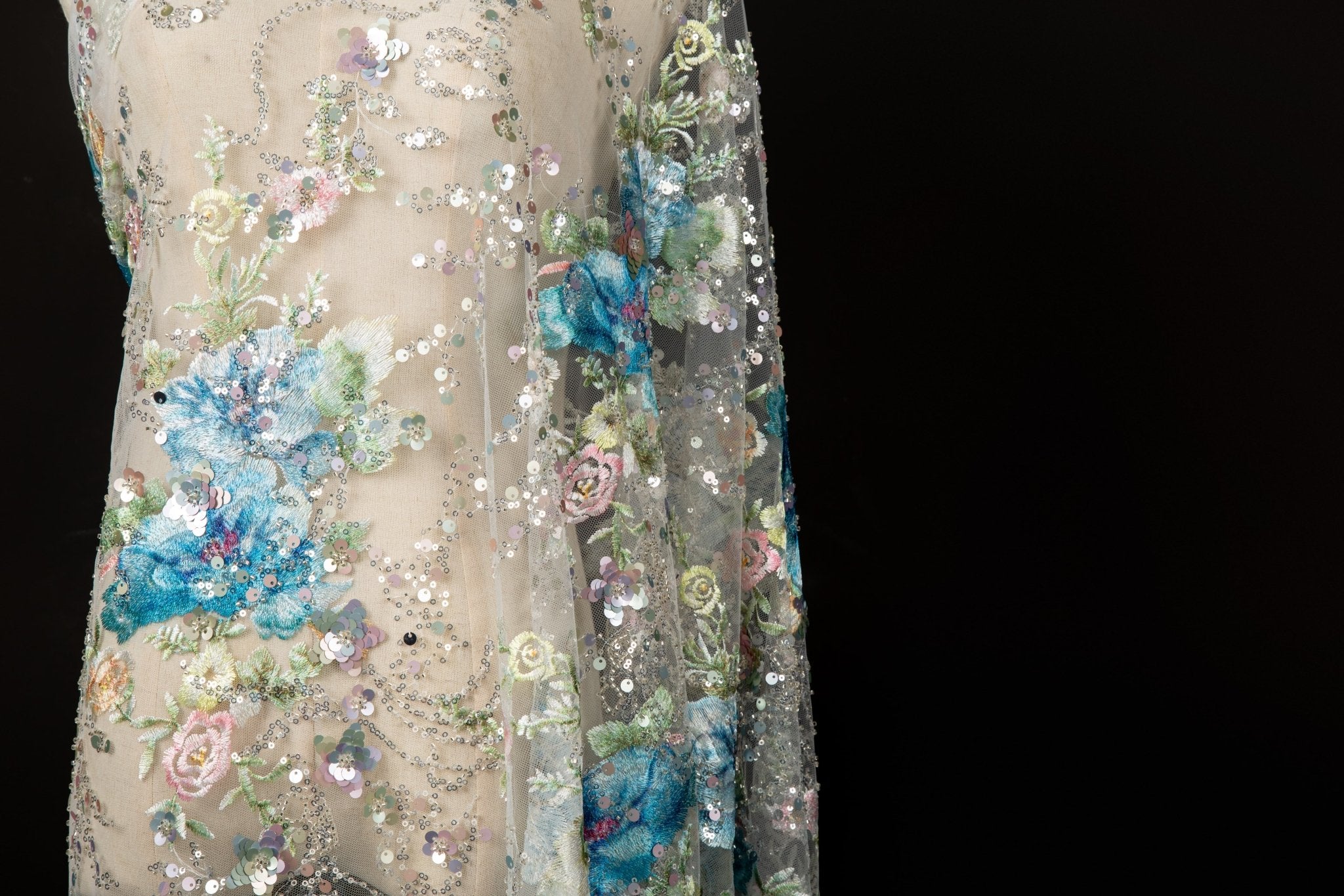  A painterly floral sequin and thread embroidery fabric on an ivory mesh base with soft pastel-colored flowers.
