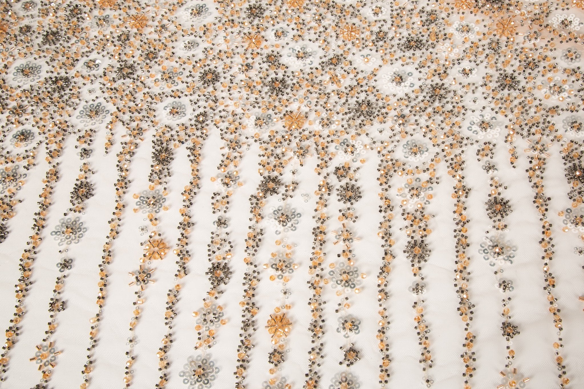 A fine beaded embroidery fabric, with a cascading stardust pattern of vertical lines in champagne gold and pewter.
