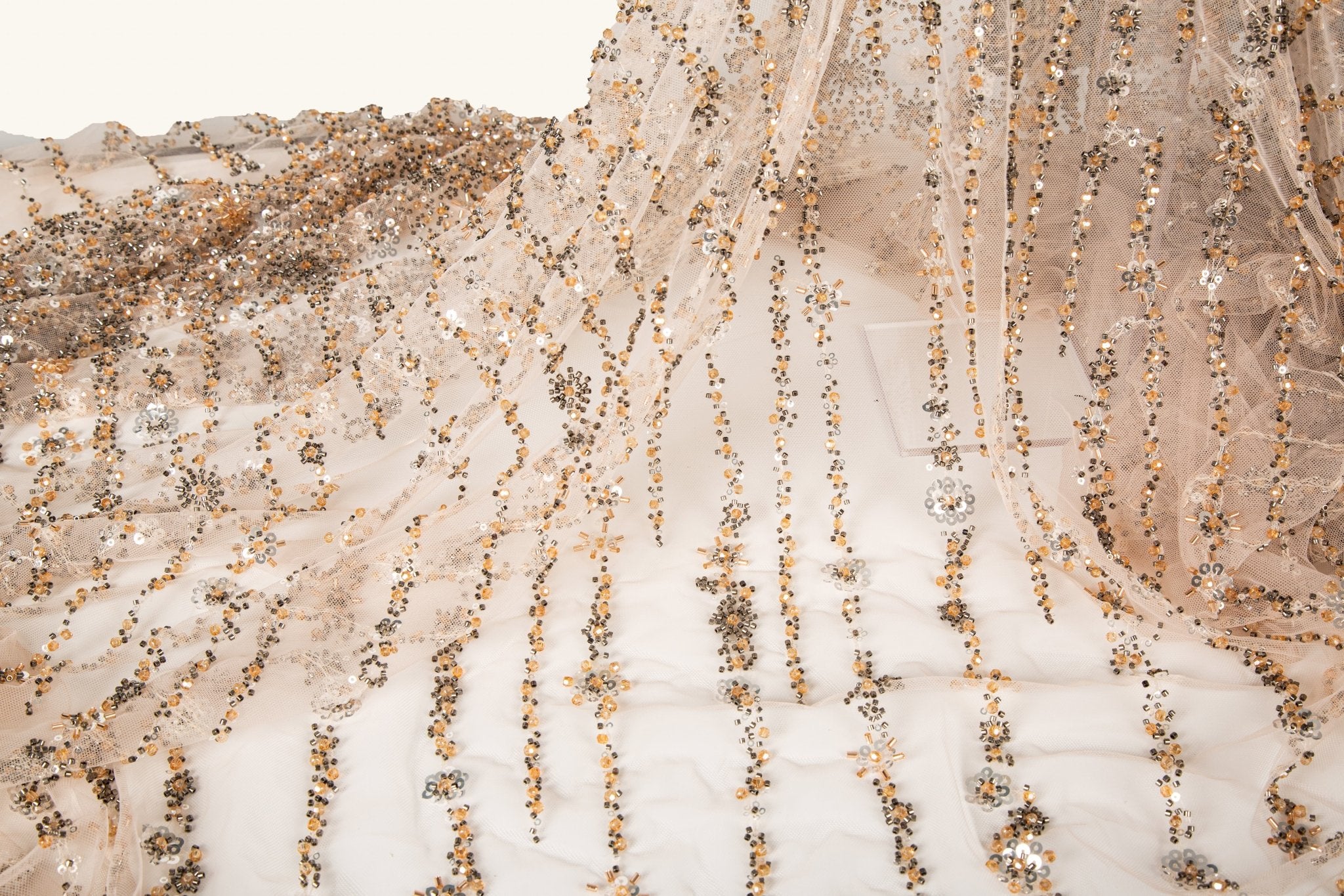 A fine beaded embroidery fabric, with a cascading stardust pattern of vertical lines in champagne gold and pewter.