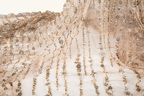 A fine beaded embroidery fabric, with a cascading stardust pattern of vertical lines in champagne gold and pewter.