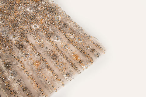 A fine beaded embroidery fabric, with a cascading stardust pattern of vertical lines in champagne gold and pewter.