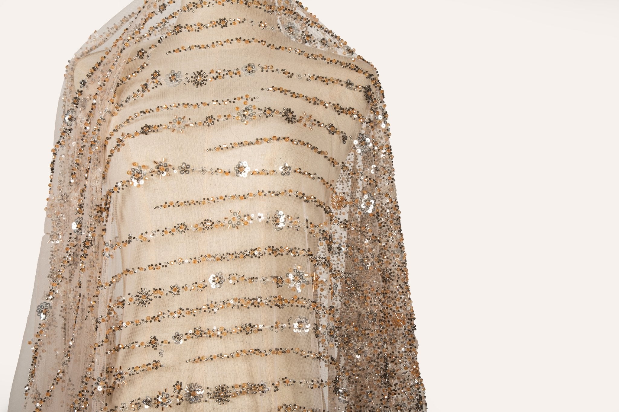 A fine beaded embroidery fabric, with a cascading stardust pattern of vertical lines in champagne gold and pewter.