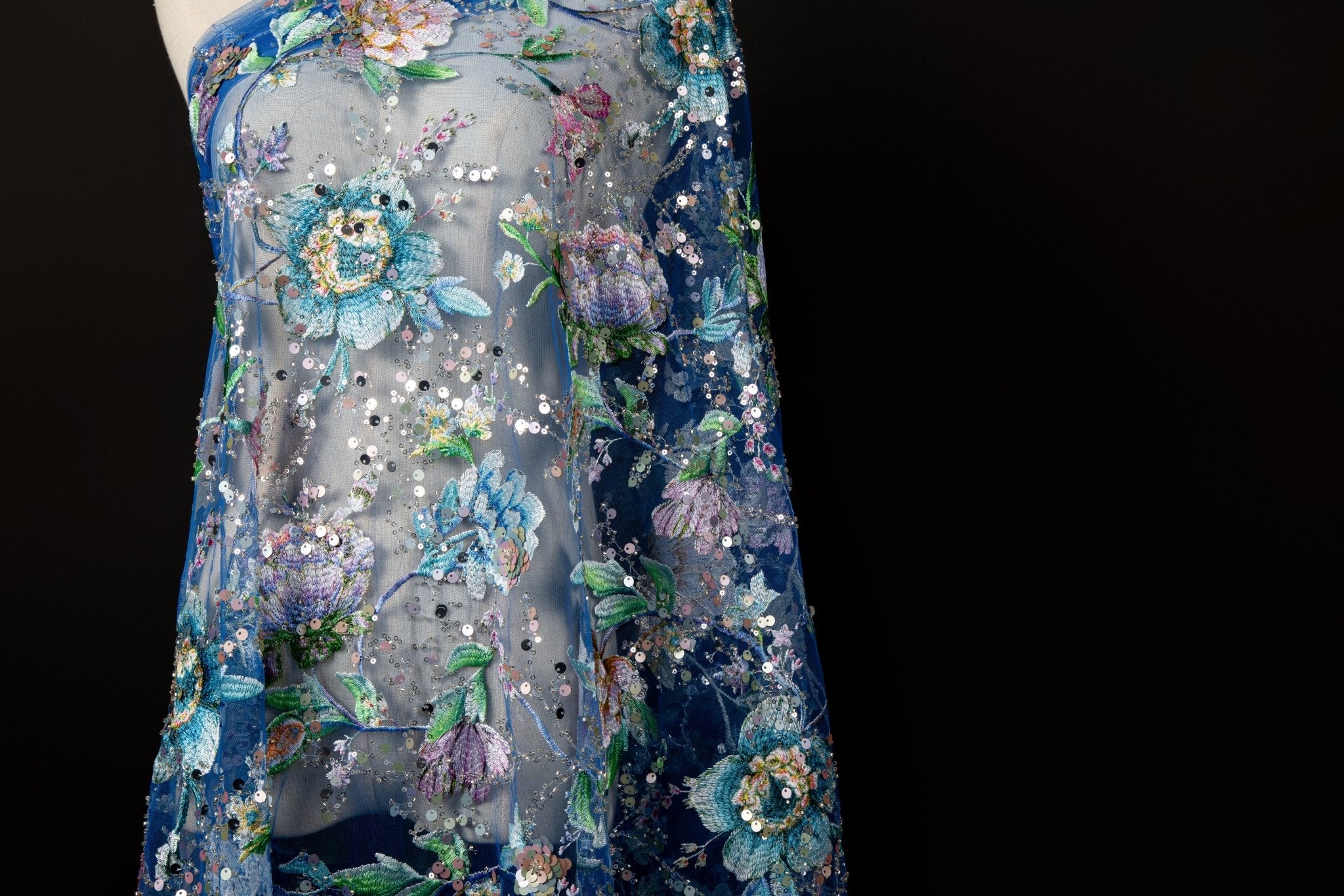 A multi-color floral sequin embroidery fabric on a sapphire blue mesh base.