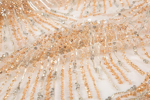 An Art Deco style beaded fabric, with a radiating palm leaf or sunburst pattern in a rose gold and silver palette.
