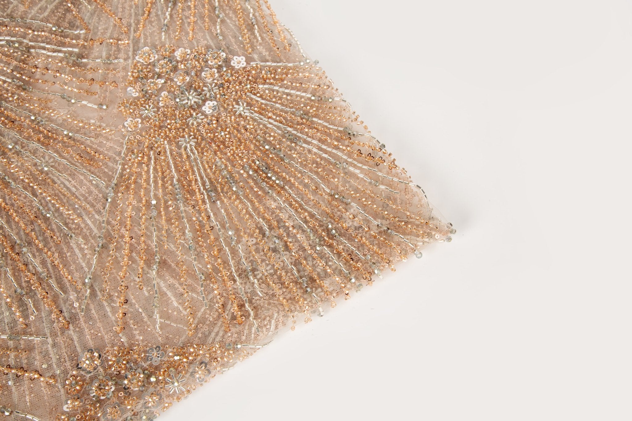 An Art Deco style beaded fabric, with a radiating palm leaf or sunburst pattern in a rose gold and silver palette.
