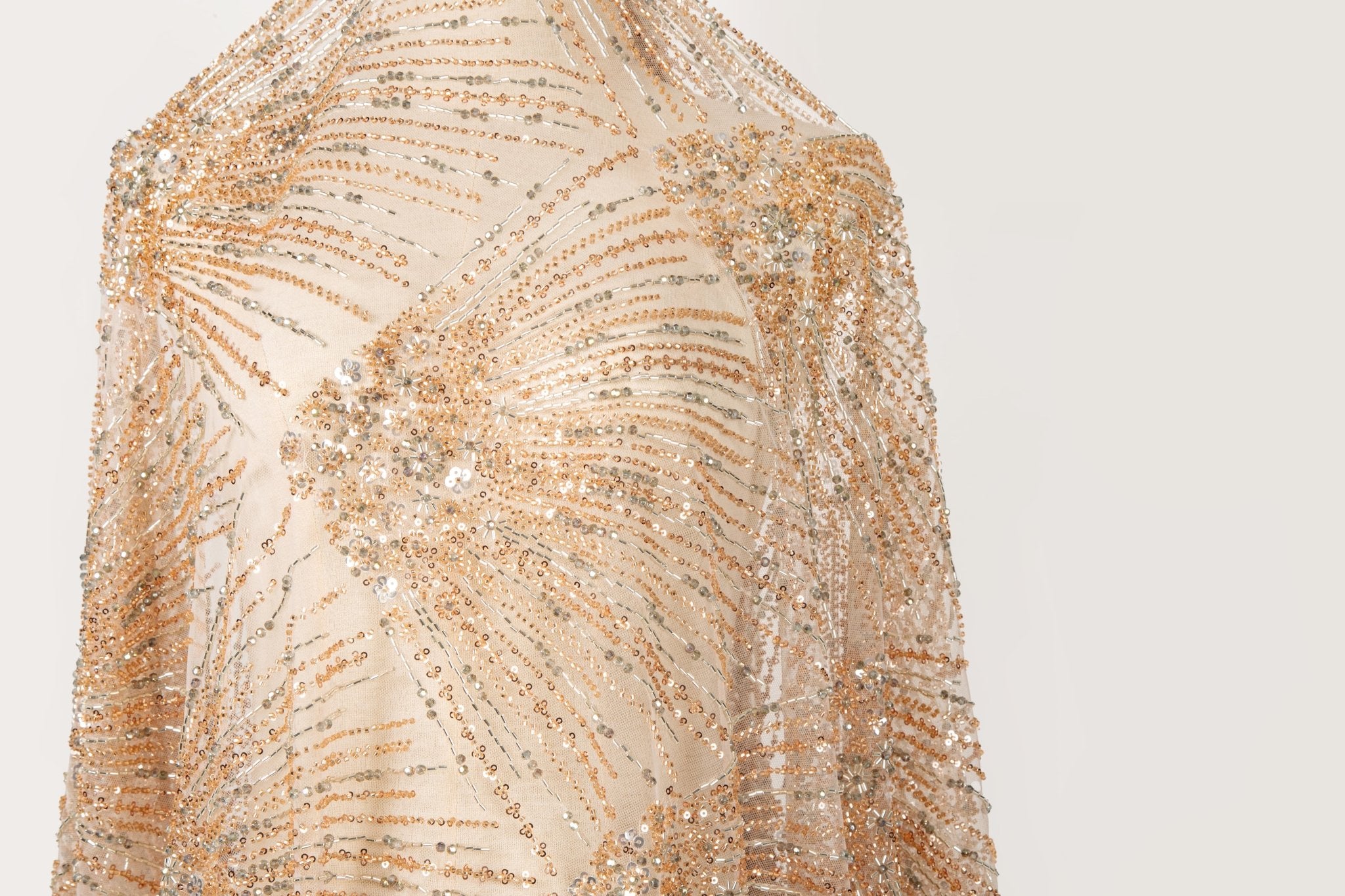 An Art Deco style beaded fabric, with a radiating palm leaf or sunburst pattern in a rose gold and silver palette.
