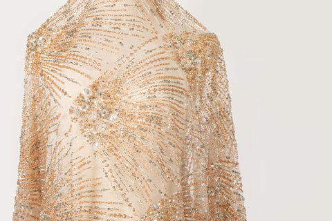 An Art Deco style beaded fabric, with a radiating palm leaf or sunburst pattern in a rose gold and silver palette.
