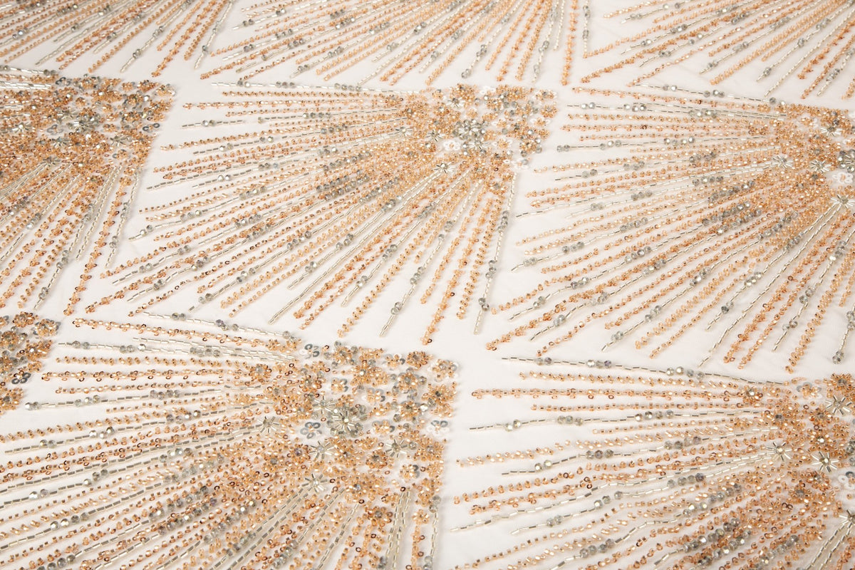 An Art Deco style beaded fabric, with a radiating palm leaf or sunburst pattern in a rose gold and silver palette.
